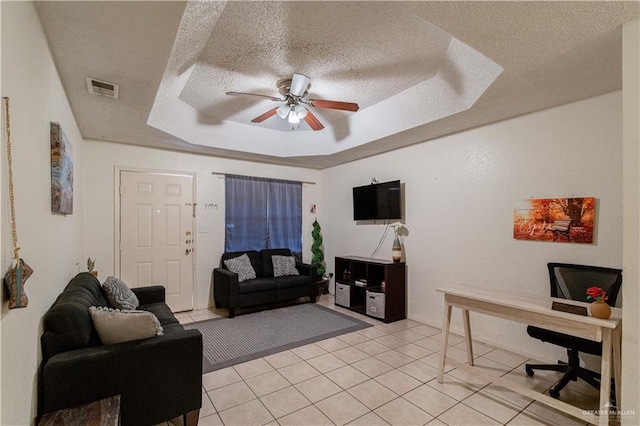 living room with a textured ceiling, a tray ceiling, and ceiling fan