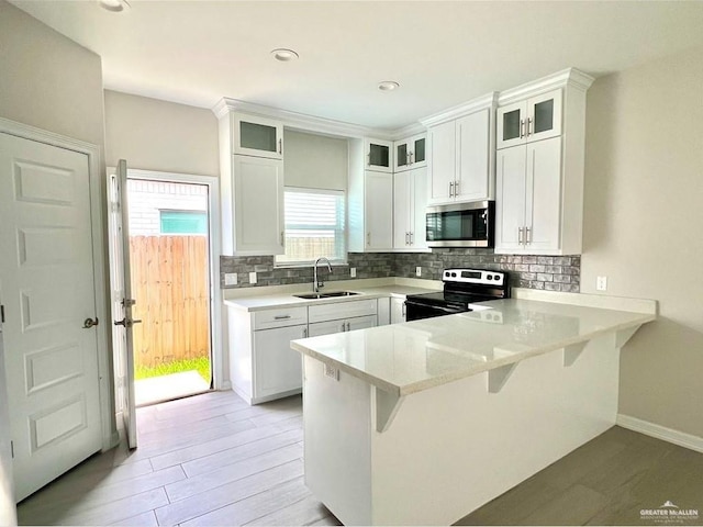 kitchen with a breakfast bar, sink, white cabinets, electric range, and kitchen peninsula