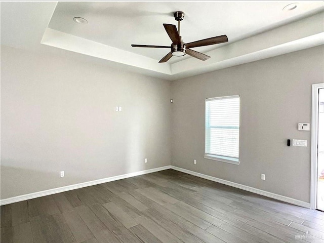 empty room featuring wood-type flooring, ceiling fan, and a tray ceiling