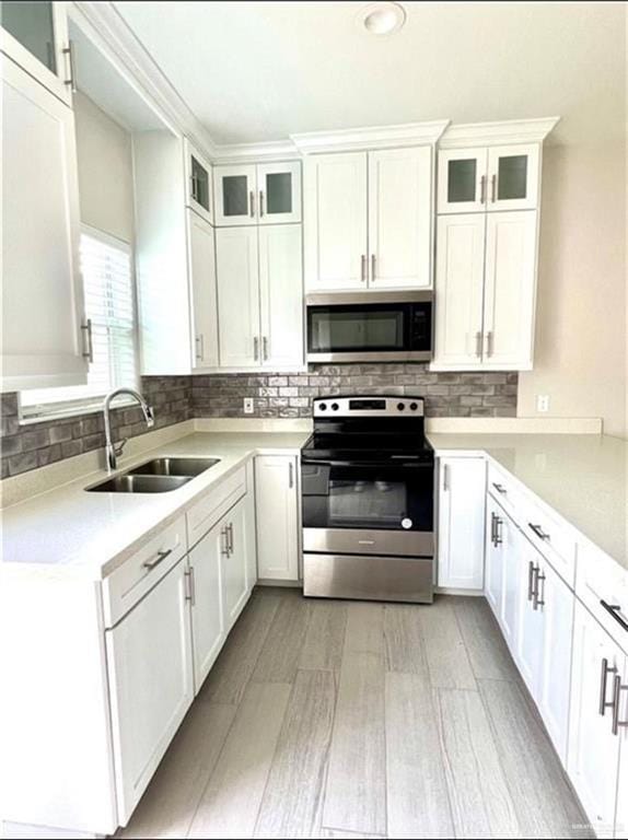 kitchen featuring sink, white cabinetry, stainless steel appliances, light hardwood / wood-style floors, and decorative backsplash