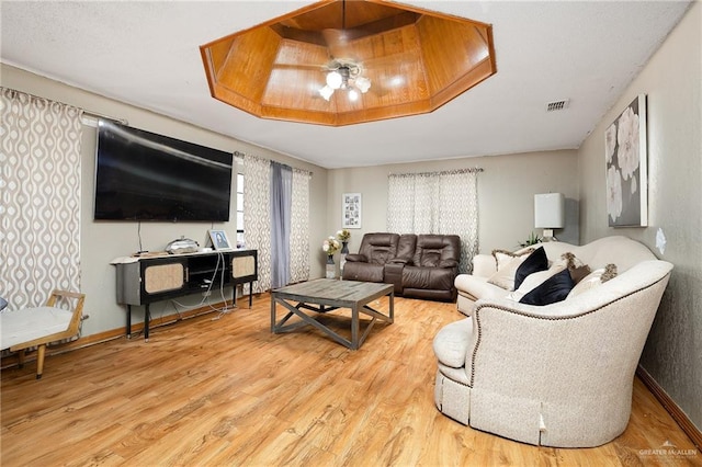 living area with baseboards, visible vents, a ceiling fan, wood finished floors, and a tray ceiling