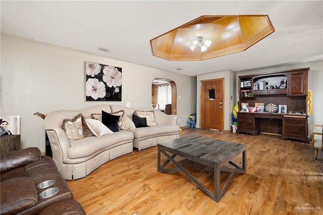 living area with arched walkways, light wood-style flooring, and visible vents