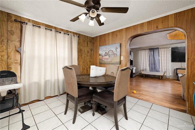 dining space with light tile patterned floors, arched walkways, ornamental molding, a textured ceiling, and wood walls