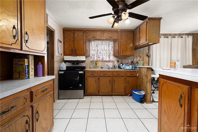 kitchen featuring electric range oven, a textured ceiling, brown cabinets, and under cabinet range hood