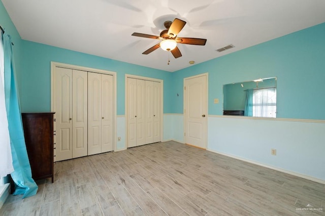 unfurnished bedroom with two closets, light hardwood / wood-style flooring, and ceiling fan