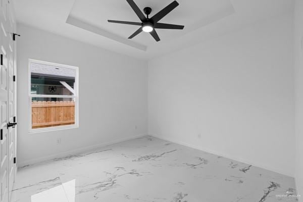 unfurnished room with ceiling fan and a tray ceiling