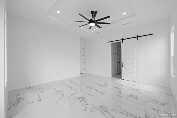 unfurnished room with ceiling fan, a barn door, and a raised ceiling