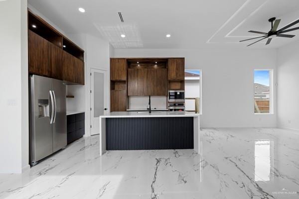 kitchen featuring dark brown cabinetry, an island with sink, ceiling fan, and appliances with stainless steel finishes