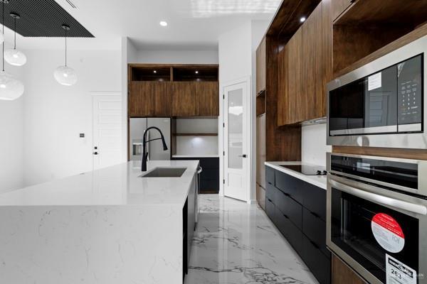 kitchen with pendant lighting, stainless steel appliances, a kitchen island with sink, and sink