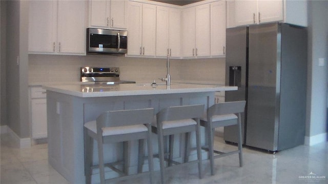 kitchen with a breakfast bar, stainless steel appliances, a kitchen island with sink, decorative backsplash, and white cabinets