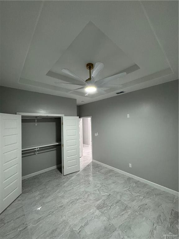 unfurnished bedroom featuring ceiling fan, a tray ceiling, and a closet