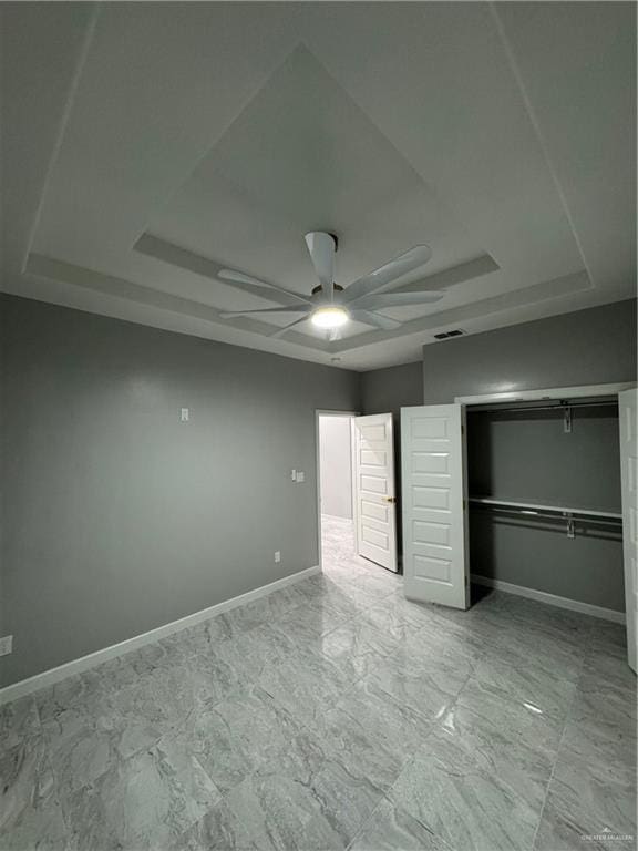 unfurnished bedroom with a tray ceiling, a closet, and ceiling fan