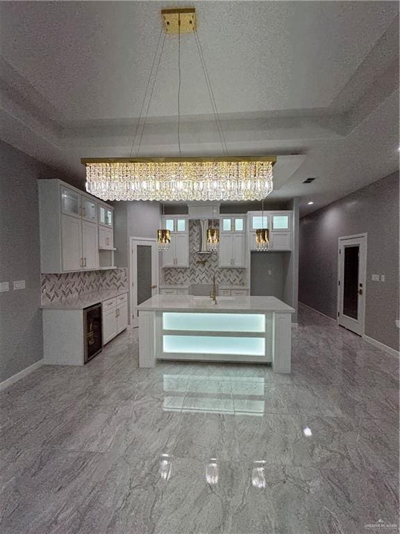 kitchen with pendant lighting, white cabinetry, a kitchen island with sink, a textured ceiling, and decorative backsplash