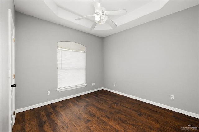 empty room with ceiling fan, dark hardwood / wood-style floors, and a raised ceiling