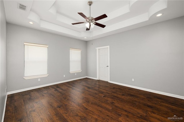 spare room with dark wood-type flooring, ceiling fan, and a raised ceiling