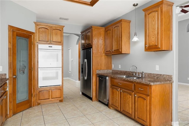 kitchen with sink, dark stone counters, light tile patterned floors, pendant lighting, and stainless steel appliances