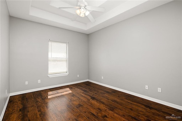 unfurnished room featuring a raised ceiling, dark hardwood / wood-style floors, and ceiling fan