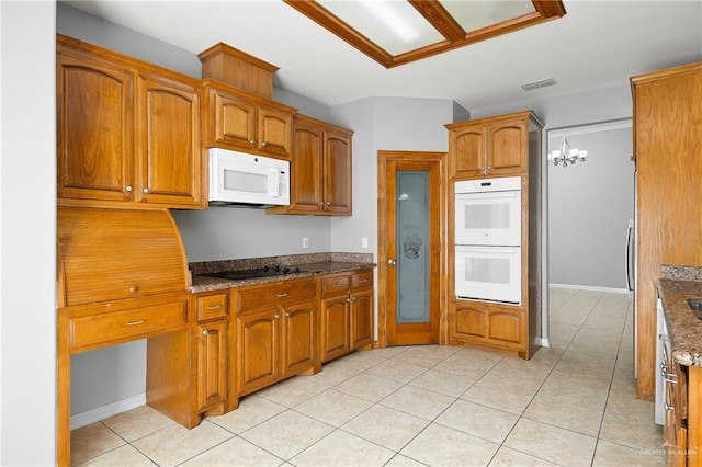 kitchen with dark stone countertops, a chandelier, white appliances, and light tile patterned flooring