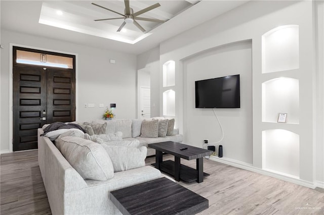 living room with ceiling fan, a raised ceiling, and light hardwood / wood-style flooring