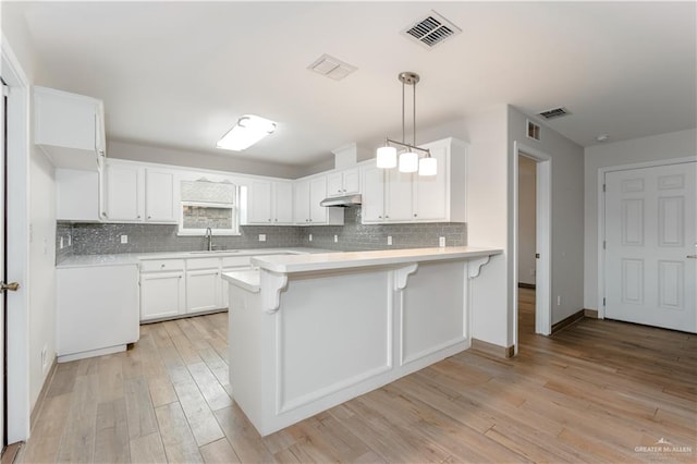 kitchen with white cabinetry, sink, light hardwood / wood-style flooring, kitchen peninsula, and pendant lighting