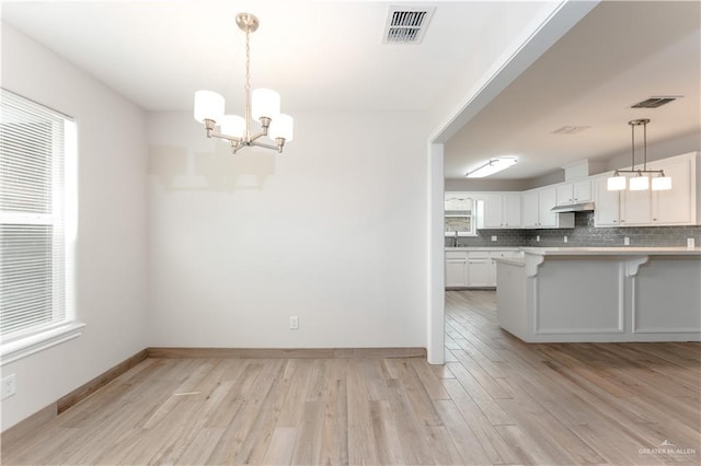 unfurnished dining area with an inviting chandelier, sink, and light hardwood / wood-style flooring