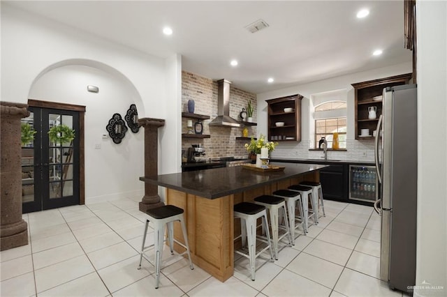 kitchen with a breakfast bar, stainless steel refrigerator, beverage cooler, and wall chimney range hood