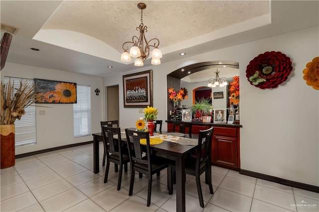 dining space with a chandelier, a raised ceiling, and light tile patterned flooring