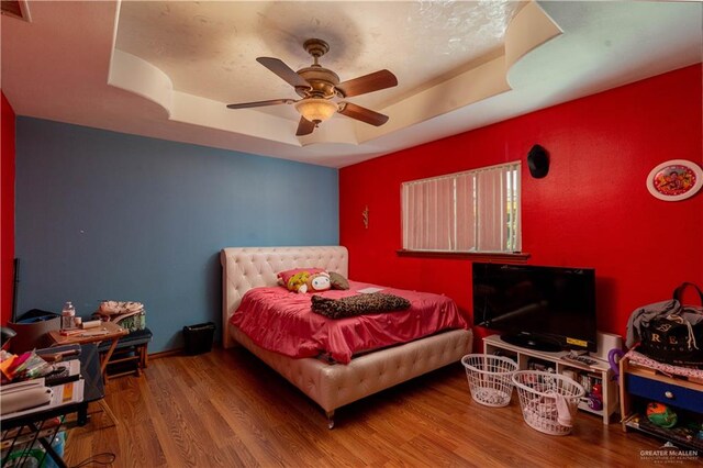 bedroom featuring a raised ceiling, ceiling fan, and hardwood / wood-style flooring