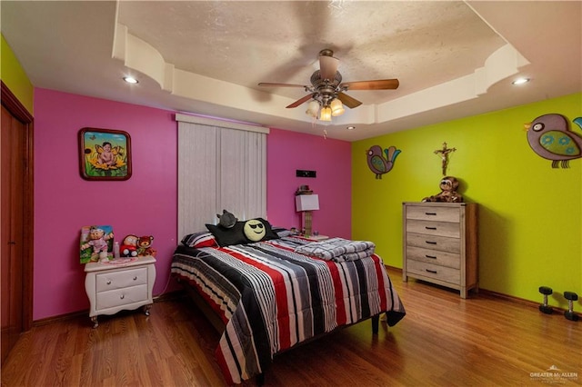 bedroom featuring wood-type flooring, a tray ceiling, and ceiling fan