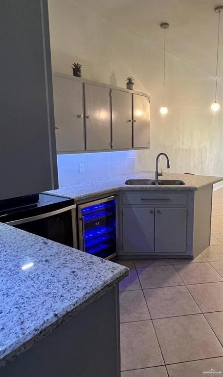 kitchen with light stone countertops, sink, beverage cooler, pendant lighting, and light tile patterned floors