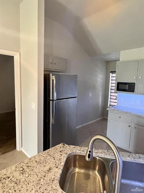 kitchen featuring lofted ceiling, sink, light stone countertops, light tile patterned floors, and stainless steel refrigerator