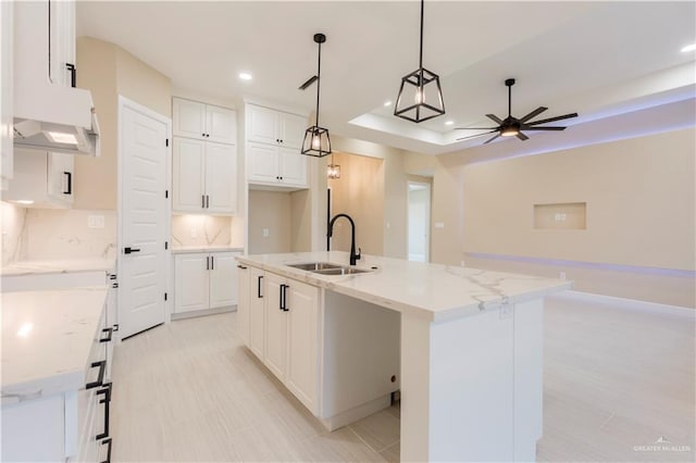 kitchen featuring white cabinets, light stone counters, an island with sink, and hanging light fixtures