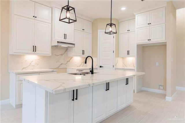 kitchen with light stone countertops, a kitchen island with sink, sink, white cabinetry, and hanging light fixtures