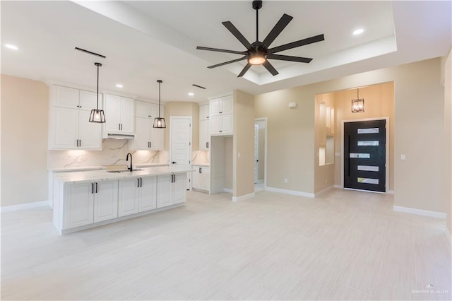 kitchen with sink, a large island with sink, pendant lighting, decorative backsplash, and white cabinets