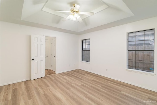 empty room with light wood-type flooring, baseboards, a tray ceiling, and ceiling fan