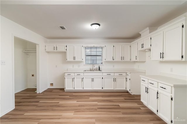 kitchen with light wood-style floors, a sink, visible vents, and white cabinets