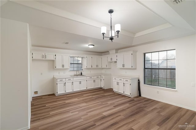 kitchen featuring a raised ceiling, a sink, white cabinets, and light wood-style floors