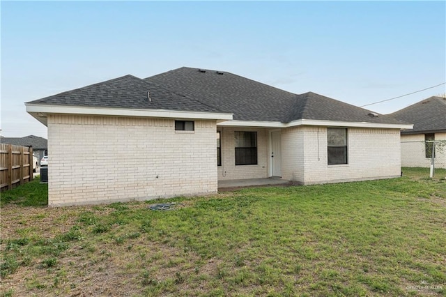 back of property featuring a yard, brick siding, fence, and a shingled roof