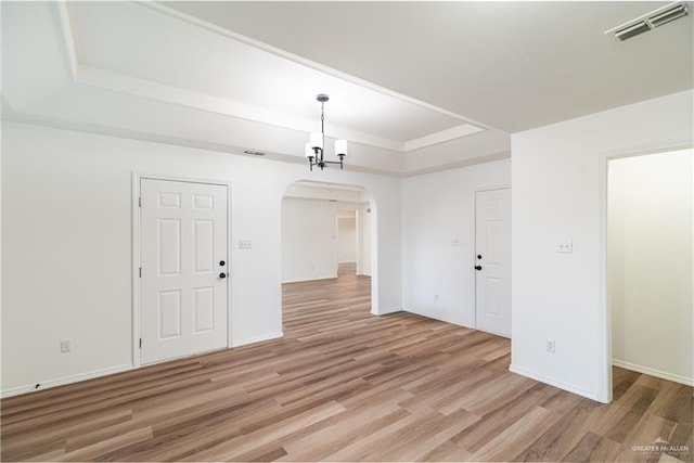 unfurnished room featuring arched walkways, a tray ceiling, visible vents, and light wood-style floors