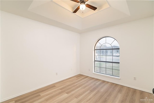 spare room featuring light wood finished floors, a raised ceiling, a ceiling fan, and baseboards