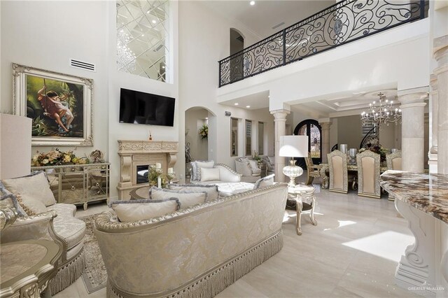 living room featuring decorative columns, a towering ceiling, light tile patterned floors, and a notable chandelier