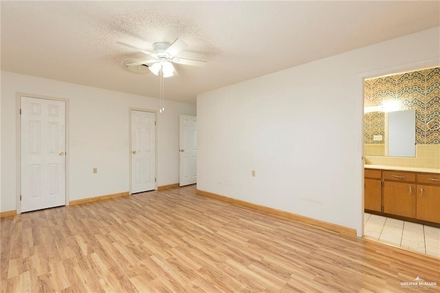 unfurnished bedroom with a textured ceiling, ceiling fan, light hardwood / wood-style flooring, and ensuite bath