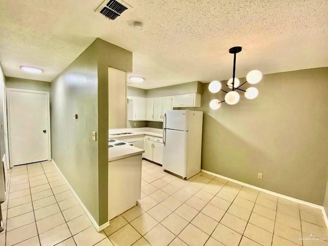 kitchen featuring a textured ceiling, light tile patterned floors, light countertops, white cabinets, and freestanding refrigerator