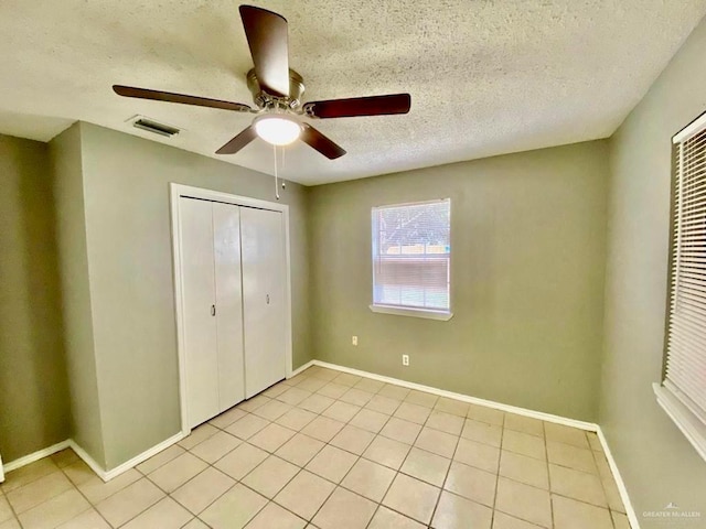 unfurnished bedroom with visible vents, a closet, a textured ceiling, a ceiling fan, and light tile patterned floors