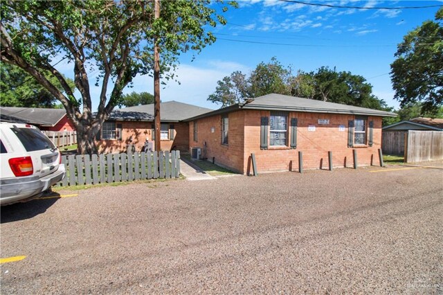 view of front facade with brick siding, fence, and central air condition unit
