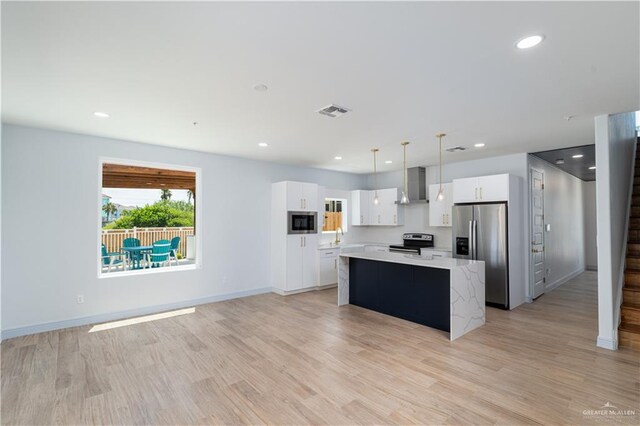 kitchen featuring appliances with stainless steel finishes, wall chimney range hood, pendant lighting, white cabinets, and a kitchen island