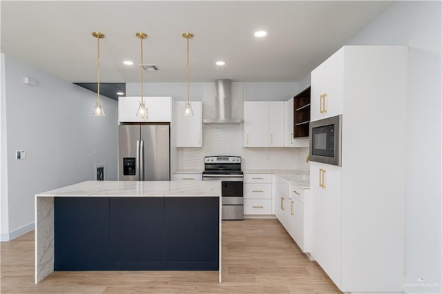 kitchen with appliances with stainless steel finishes, wall chimney exhaust hood, light hardwood / wood-style floors, white cabinetry, and hanging light fixtures