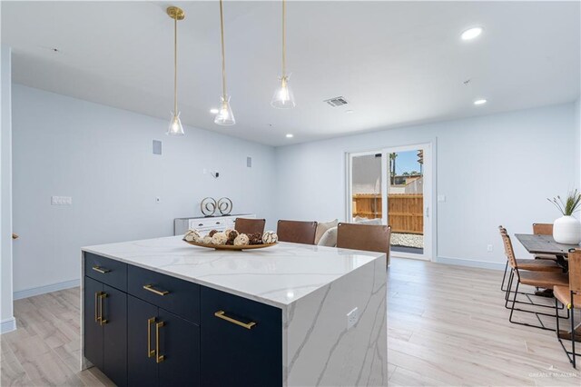 kitchen with light stone countertops, pendant lighting, a center island, and light hardwood / wood-style flooring