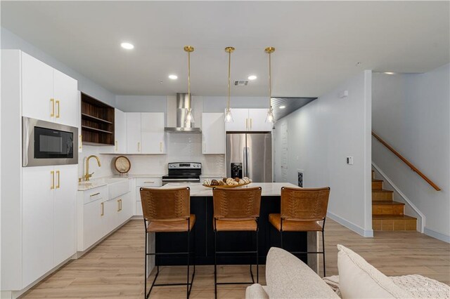 kitchen featuring pendant lighting, a center island, wall chimney exhaust hood, white cabinetry, and stainless steel appliances