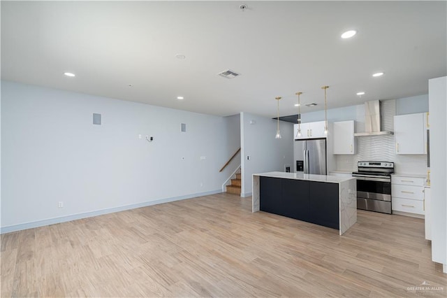 kitchen with white cabinets, wall chimney range hood, hanging light fixtures, appliances with stainless steel finishes, and a kitchen island